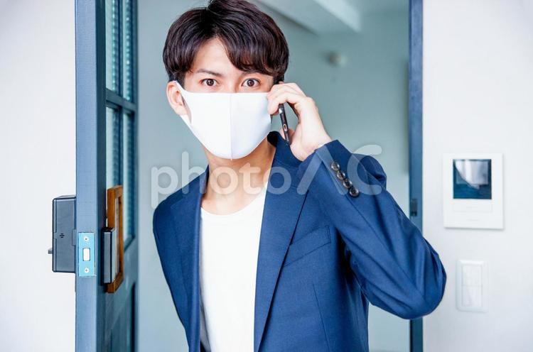 マスクをしてドアから電話して入ってくる男性 マスク,スマホ,コロナ対策の写真素材