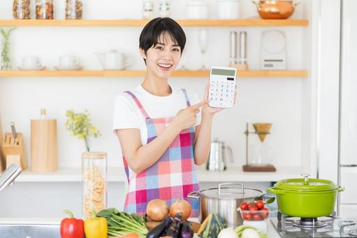 キッチンで電卓を持つ主婦。 キッチンで電卓を持つ主婦。の写真