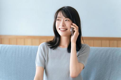 ソファに座ってスマホで話す笑顔の女性 ソファに座ってスマホで話す笑顔の女性 女性,スマホ,スマートフォンの写真素材