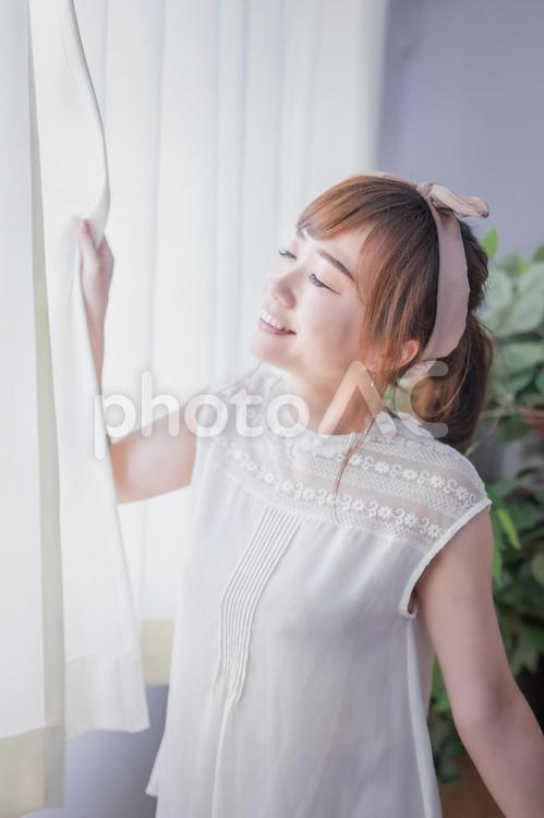 カーテンから差し込む朝日を浴びる若い女性 朝日,深呼吸,窓の写真素材