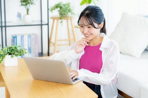 自宅でノートパソコンを操作する若い女性 自宅でノートパソコンを操作する若い女性 若い女性,ノートパソコン,笑顔の写真素材