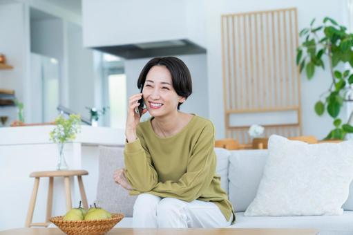 リビングで電話するミドルの女性 リビングで電話するミドルの女性の写真