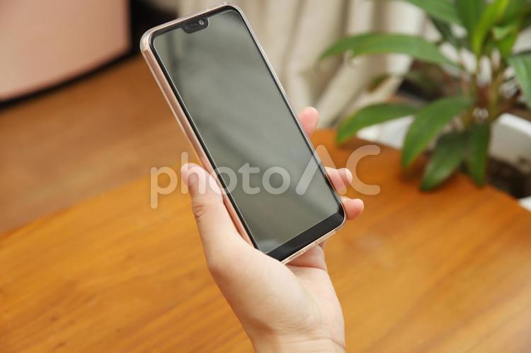 スマホを握る女性の手と観葉植物と木目の机 スマホ,女性,手の写真素材