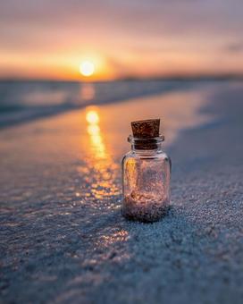 夕焼けのビーチに佇む、砂入りのガラス瓶 夕焼けのビーチに佇む、砂入りのガラス瓶の写真