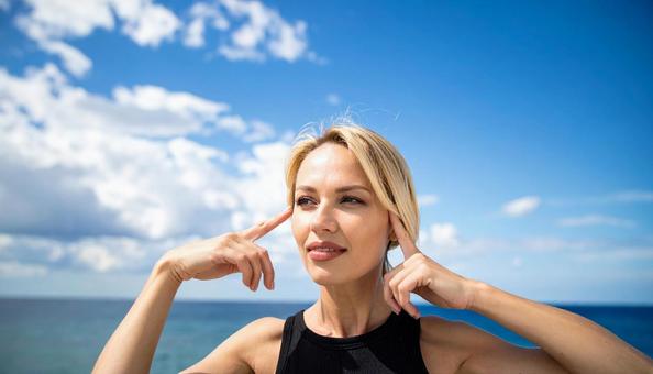 青空と頭に手を指さす女性の写真