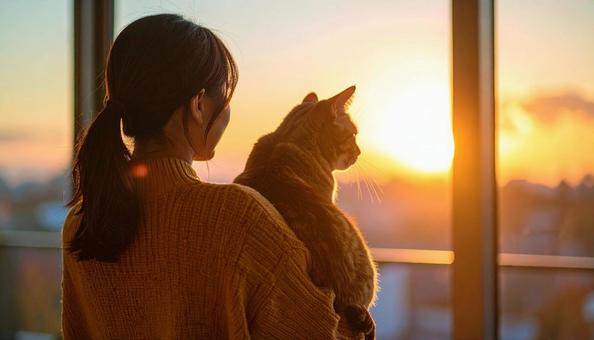 室内でネコを抱いて窓から景色を眺める女性 室内でネコを抱いて窓から景色を眺める女性の写真
