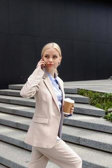 オフィスビルの外の階段でコーヒー片手に電話している金髪のビジネスウーマン ビジネスウーマン,ビジネス,女性の写真素材