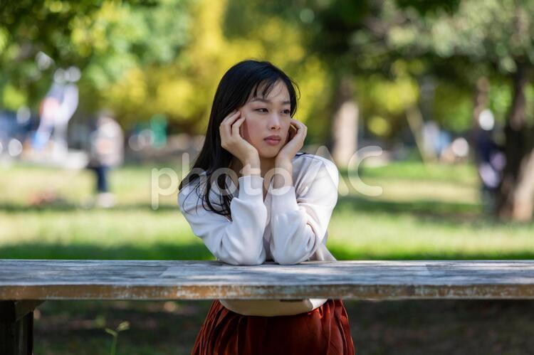 公園のベンチに座り頬杖をつく長い髪の女性 女性,公園,若いの写真素材