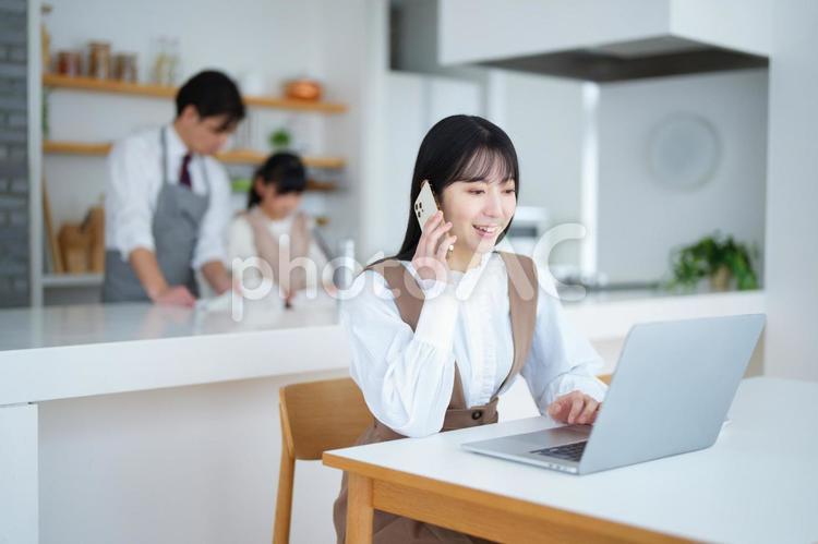 電話する女性と後ろで皿洗いする男性と女の子 家族,女の子,女性の写真素材