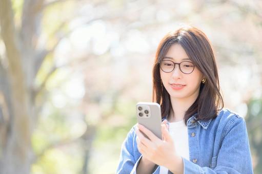 公園でスマホを見るメガネの女性 公園でスマホを見るメガネの女性 人物,女性,笑顔の写真素材