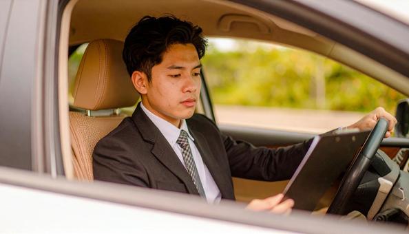 手もとに書類を持って運転するサラリーマン 手もとに書類を持って運転するサラリーマンの写真