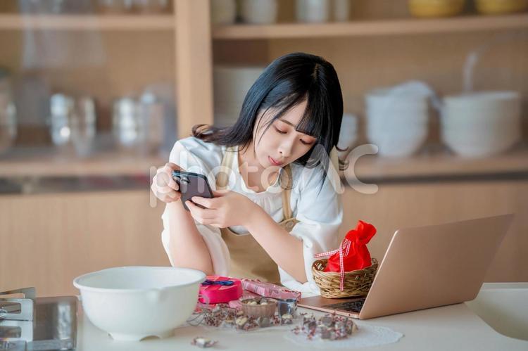 携帯を見て仕事をさぼる若い女性料理人 バレンタイン,バレンタインデー,チョコの写真素材
