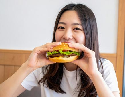 おいしそうにハンバーガーにかじりつく女性 おいしそうにハンバーガーにかじりつく女性の写真