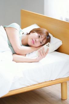 横になりながらスマホを見る女性 女性,スマートフォン,持つの写真素材