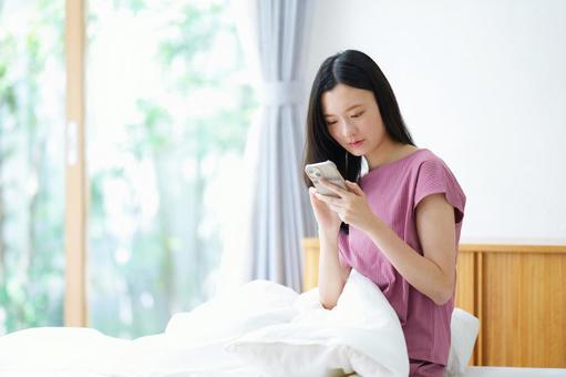 ベッドで真剣な顔でスマホを操作する女性 女性,スマートフォン,持つの写真素材