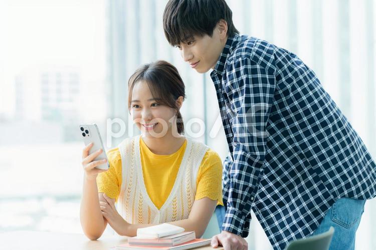 スマホを見ながら話す学生たち 大学生,スマホ,教室の写真素材