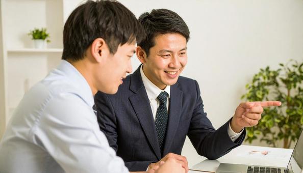 パソコンを見ながら打ち合わせをする男性の写真