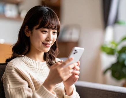 自宅のリビングでスマホを操作する女性 自宅のリビングでスマホを操作する女性の写真