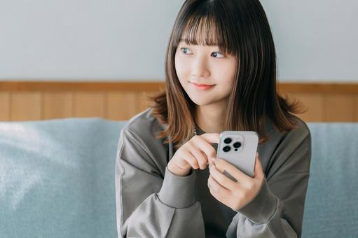 ソファに座ってスマホを使う女性 女性,スマホ,スマートフォンの写真素材