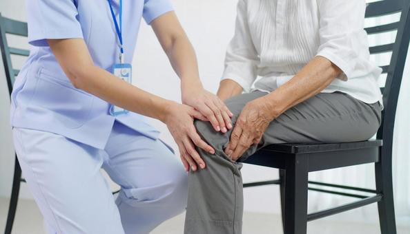 シニア女性の膝をマッサージする白衣の女性の写真