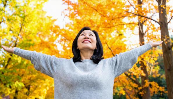 紅葉の中で深呼吸する秋服の日本人女性 紅葉の中で深呼吸する秋服の日本人女性の写真