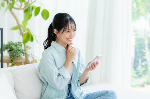部屋でスマホを操作する若い女性 スマホ,笑顔,女性の写真素材