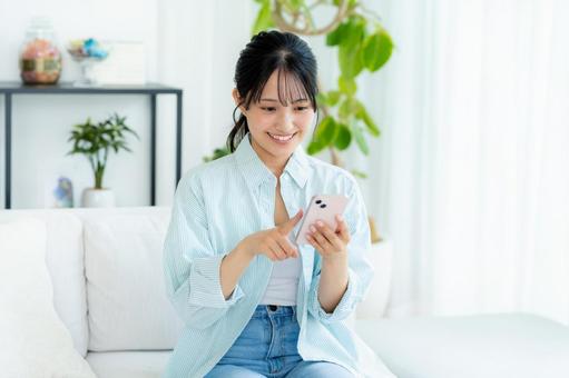 部屋でスマホを操作する若い女性 スマホ,笑顔,女性の写真素材