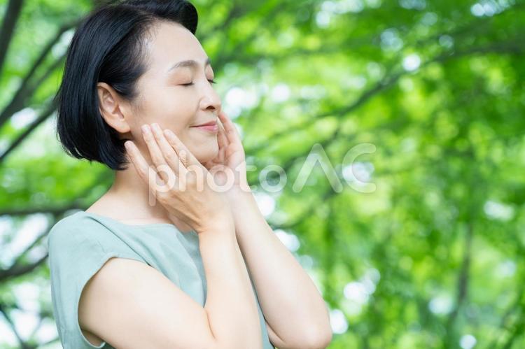 新緑の中でスキンケアをするミドルの女性 ビューティー,女性,スキンケアの写真素材