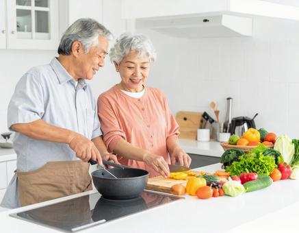 キッチンで会話しながら料理するシニア夫婦の写真