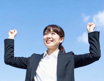 青空の下ガッツポーズする女性社員の写真