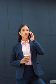 オフィスビルの外でコーヒー片手に電話する外国人女性 ビジネスウーマン,ビジネス,女性の写真素材