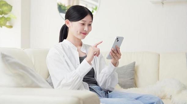 リビングでスマホを操作するアジア人女性 リビングでスマホを操作するアジア人女性 スマートフォン,操作,女性の写真素材
