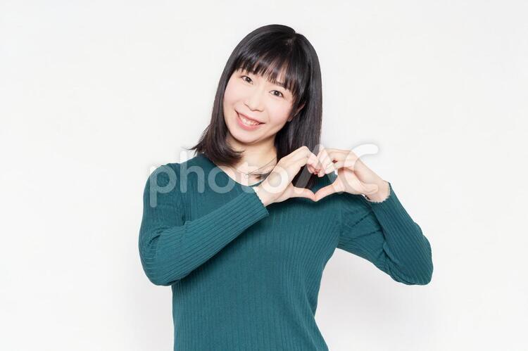 白背景の前に立って、手でハートの形を作る女性 女性,ハート,愛の写真素材