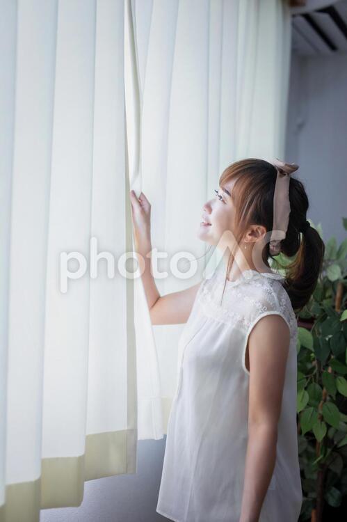 白いカーテンから差し込む朝日を浴びる若い女性 窓,横顔,女性の写真素材