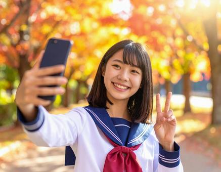 秋の並木道でスマホの自撮りをする女子高生 秋の並木道でスマホの自撮りをする女子高生の写真