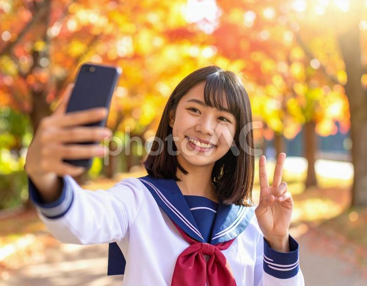 秋の並木道でスマホの自撮りをする女子高生 女子高生,秋,並木道の写真素材