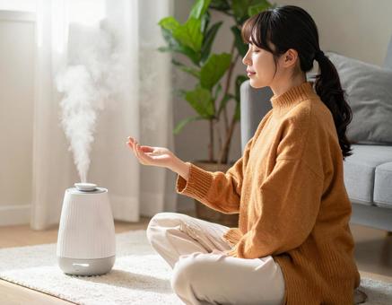 加湿器のそばでスキンケアをする女性 加湿器のそばでスキンケアをする女性の写真