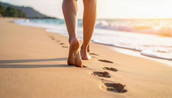 波打ち際の砂浜に足あとと白い女性の足 波打ち際の砂浜に足あとと白い女性の足の写真