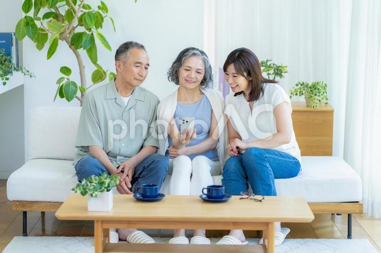 リビングでスマホを見るシニア夫婦と子供 シニア,夫婦,スマホの写真素材