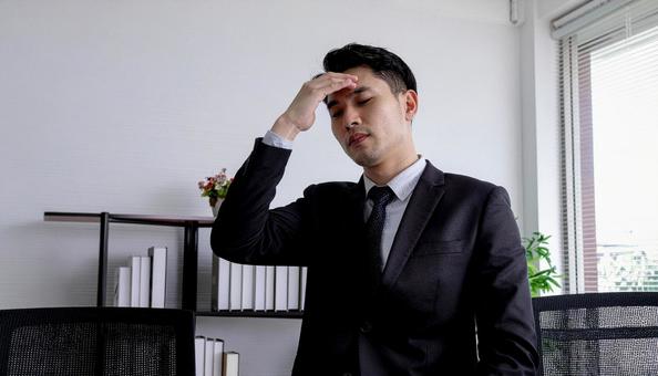 手を額に当てて苦悩するサラリーマンの写真