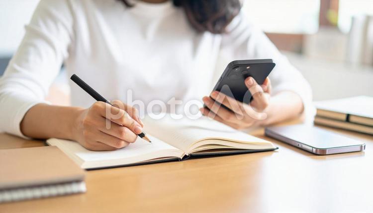 スマホ片手にノートに字を書く女性の手元 書く,手,ノートの写真素材