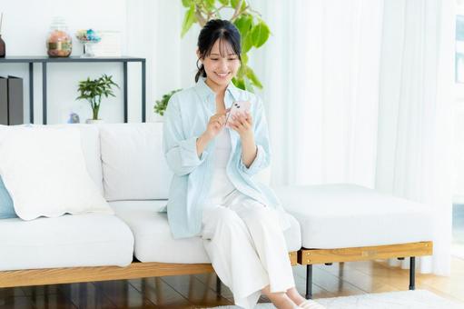 部屋でスマホを操作する若い女性 スマホ,笑顔,女性の写真素材