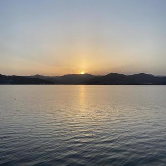 湖の対岸の山に夕陽があと少しで沈む 湖の対岸の山に夕陽があと少しで沈むの写真