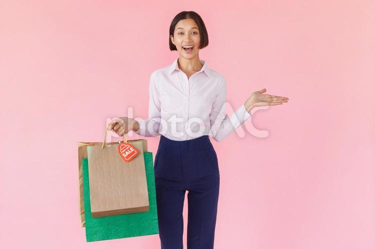 たくさんの紙袋を持っているカメラ目線の笑顔の女性（ピンク背景） セール,ショップ,女性の写真素材