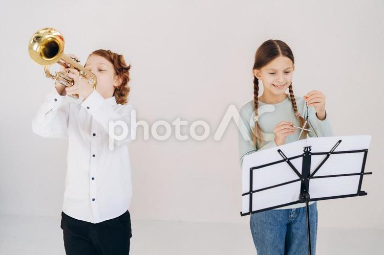 トランペットをかっこよく演奏する男の子と楽譜を見てトライアングルを演奏する女の子 女の子,男の子,人物の写真素材