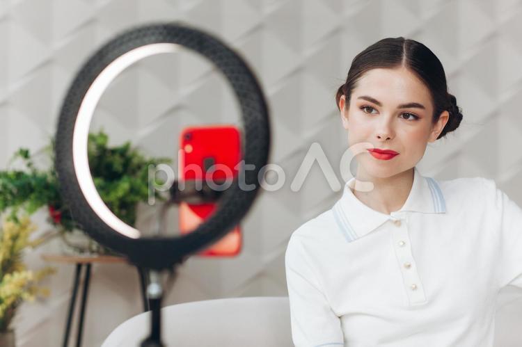 無表情で配信する女性と観葉植物 女性,ポロシャツ,赤の写真素材
