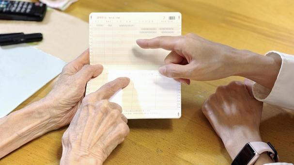 通帳を指さす高齢女性と女性の指先_俯瞰 通帳を指さす高齢女性と女性の指先_俯瞰の写真