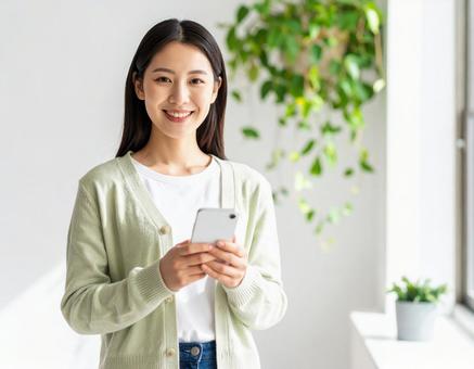 室内でスマートフォンを持つ笑顔の女性 室内でスマートフォンを持つ笑顔の女性の写真