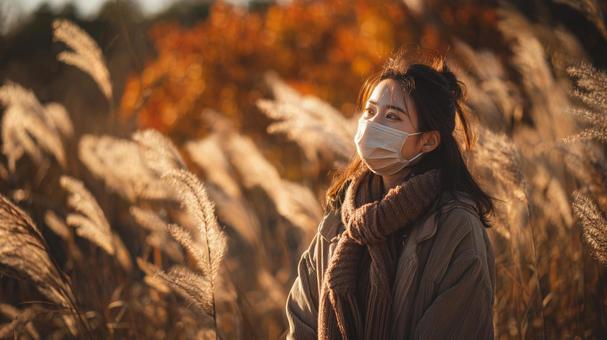 秋風に揺れるススキとマスク姿の女性 秋風に揺れるススキとマスク姿の女性の写真