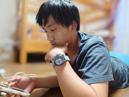 うつ伏せでスマホをイジる男性 うつ伏せでスマホをイジる男性の写真